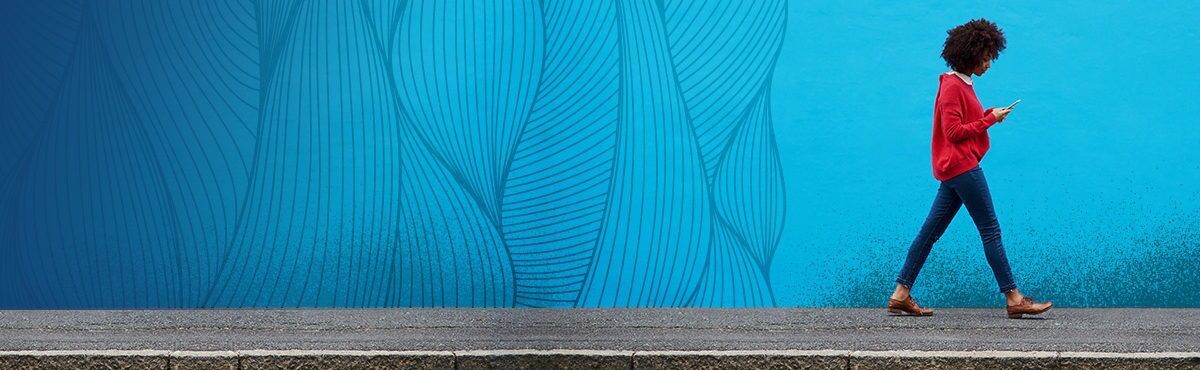 A gen z woman walks on a sidewalk in front of a bright blue wall with an organic strand texture. The woman and texture represent the relationship of buyer needs and expectations and a seller's capacity for success through honoring the customer.